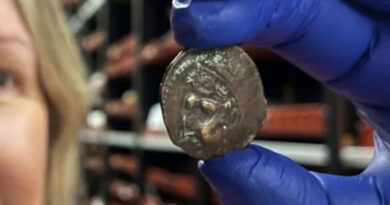 Busfahrgeld. Eine lächelnde Frau mit einem blauen Latexhandschuh, die eine kleine Bronzemünze zwischen Daumen und Zeigefinger hält. Bild: Leeds Museums and Galleries