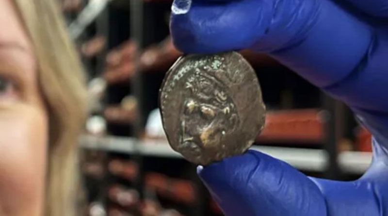 Busfahrgeld. Eine lächelnde Frau mit einem blauen Latexhandschuh, die eine kleine Bronzemünze zwischen Daumen und Zeigefinger hält. Bild: Leeds Museums and Galleries